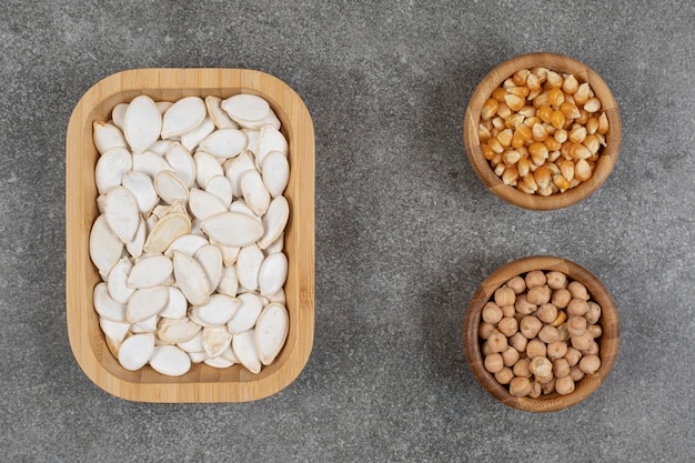 Graines de citrouille savoureuses, grains de maïs et pois sur marbre.