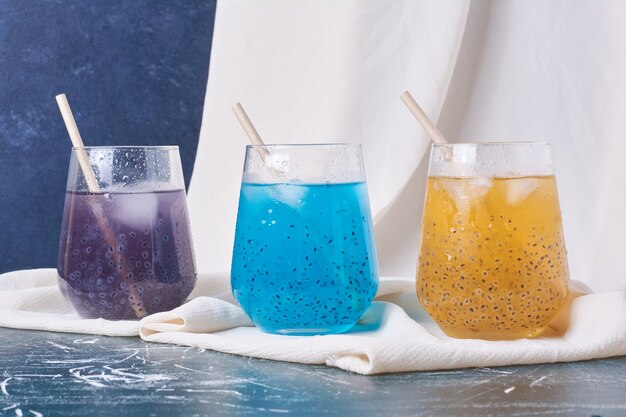 Graines de fruits avec des tasses de boisson colorées sur bleu.