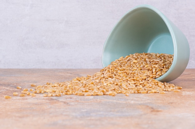 Grains de blé secs dans un bol renversé, sur le marbre.