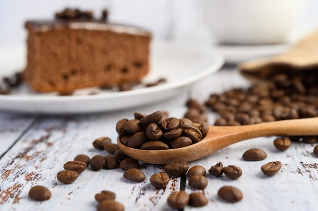 Grains de café sur une cuillère en bois sur une table en bois blanc.