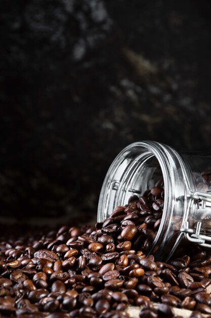 Grains de café dans un bocal en verre sur fond noir gros plan mise au point sélective cadre vertical Torréfaction et préparation du cadre vertical du café