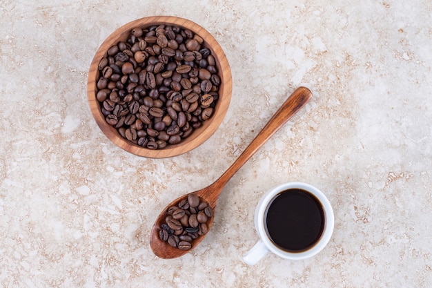 Grains de café dans un bol et sur une cuillère à côté d'une tasse de café