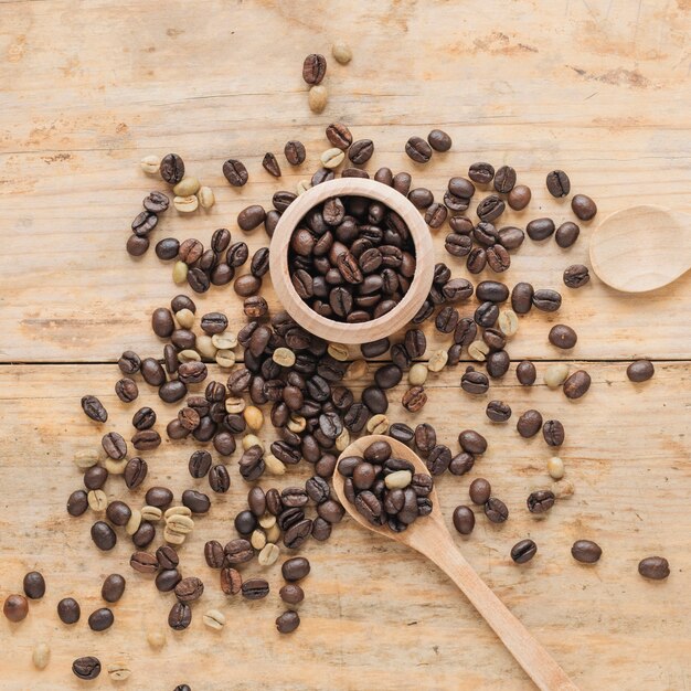 Grains de café dans un récipient en bois et sur la table avec une cuillère