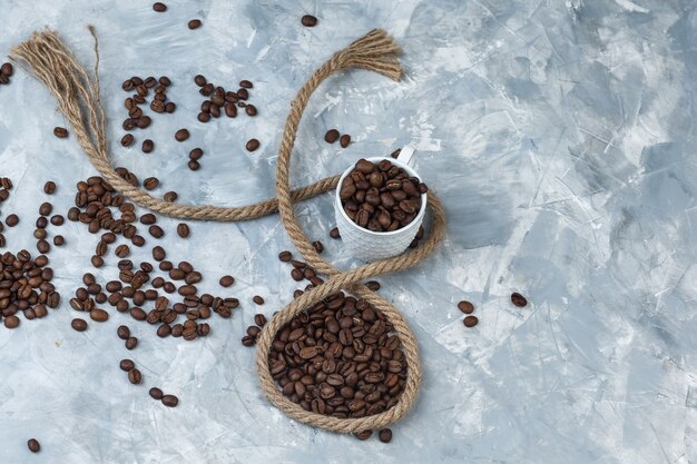 Les grains de café dans une tasse blanche avec une corde à plat poser sur un fond de plâtre gris