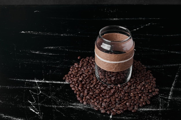 Grains de café sur fond noir et dans le bocal en verre.