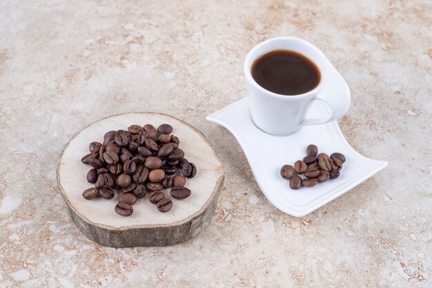 Grains de café sur une planche de bois et un plateau à côté d'une tasse de café infusé