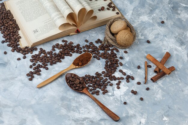 Grains de café à plat, café instantané dans des cuillères en bois avec livre, cannelle, biscuits, cordes sur fond de marbre bleu foncé et clair. horizontal