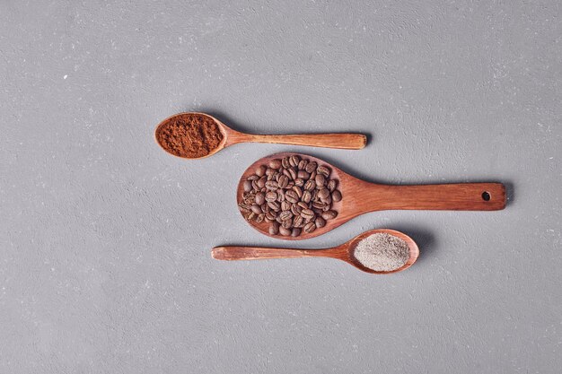 Grains de café et poudres dans des cuillères en bois.