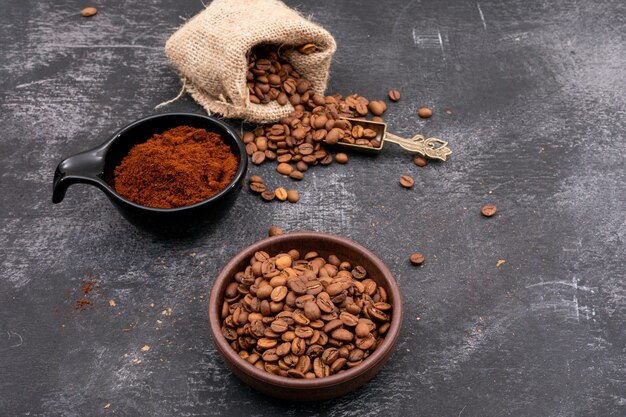 Grains de café torréfiés dans un bol en céramique et un sac et de la poudre de café sur une table sombre