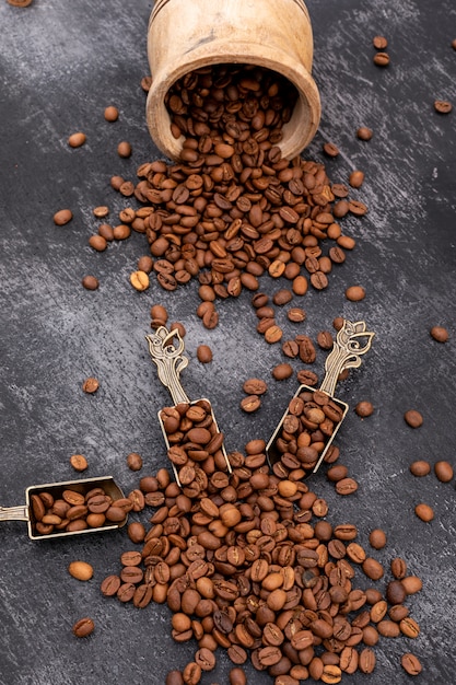 Grains de café torréfiés dans une cuillère en métal sur une surface noire