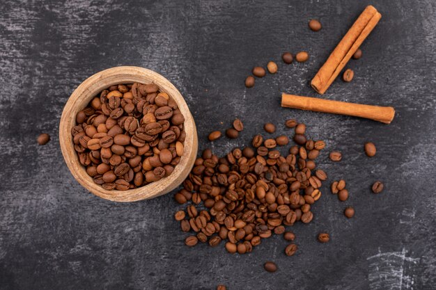 Grains de café torréfiés dans un petit bol en bois et cannelle sur une surface noire