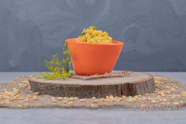 Grains de maïs dans un bol orange sur plaque en bois.