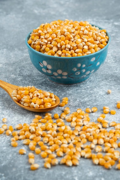 Grains de maïs non cuits dans un bol bleu sur une surface en marbre.