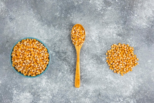 Grains de maïs non cuits dans un bol bleu sur une surface en marbre.