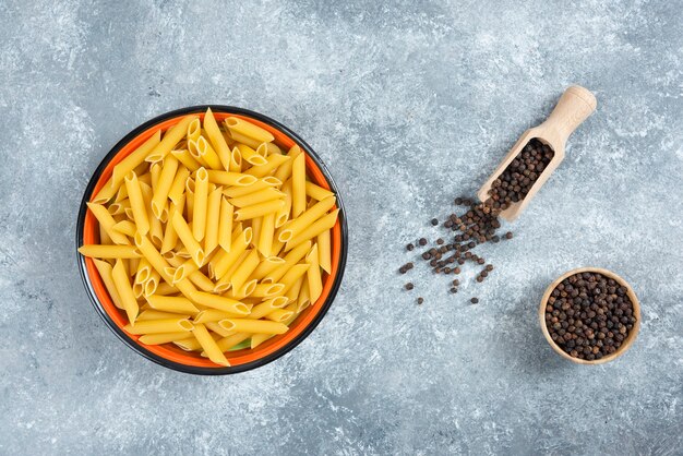 Grains de penne et de poivre crus sur fond de marbre.