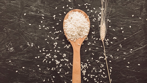 Grains de riz blanc sur une cuillère en bois sur fond gris rugueux