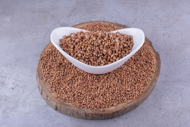 Grains de sarrasin étalés sur une planche de bois autour d'un bol de sarrasin cuit sur fond de marbre. photo de haute qualité