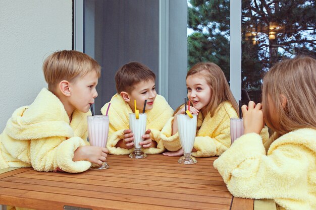 Grand groupe d'amis prenant le temps de goog avec des cocktails au lait. Heureux garçons souriants et girs en robes de chambre éponge jaune. Concept de mode pour enfants