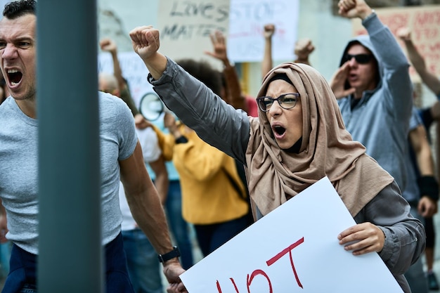 Photo gratuite grand groupe multiethnique de personnes protestant contre le racisme dans les rues l'accent est mis sur une femme moyen-orientale en colère criant avec le poing levé