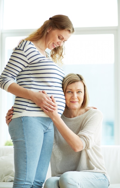 grand-mère heureuse ventre d&#39;une femme enceinte tenant