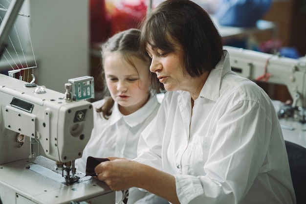 Grand-mère avec petite-fille coudre des vêtements dans l'usine