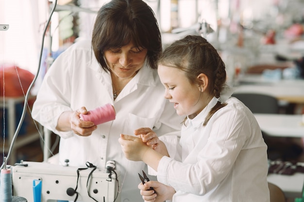 Grand-mère avec petite-fille coudre des vêtements dans l'usine