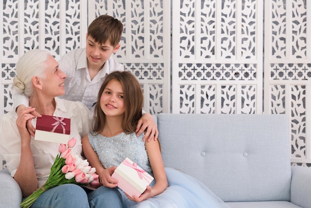 Grand-mère avec ses petits-enfants tenant une boîte-cadeau et un bouquet de fleurs