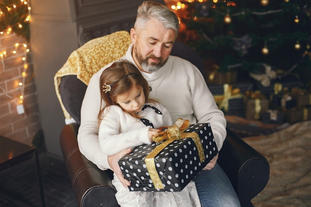 Grand-père assis avec sa petite-fille. Célébrer Noël dans une maison chaleureuse. Homme dans un pull en tricot blanc.
