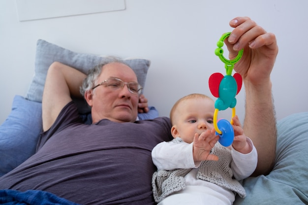 Grand-père paisible jouant avec bébé, tenant jouet hochet