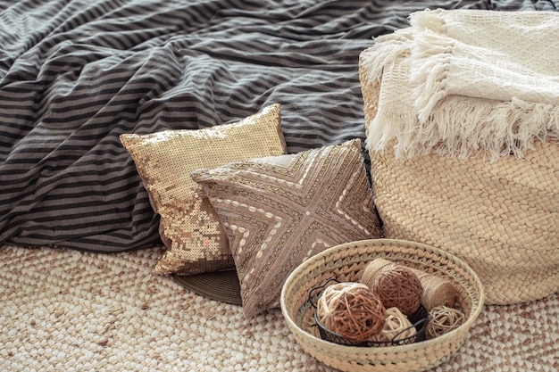 Grand sac en paille en osier, oreillers et éléments décoratifs sur fond de lit.