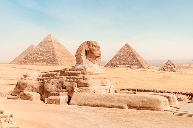 Le grand sphinx avec le corps d'un lion et le visage d'un pharaon se trouve sur le sable dans le contexte de toutes les célèbres pyramides de gizeh sous un ciel ensoleillé. le caire, egypte.