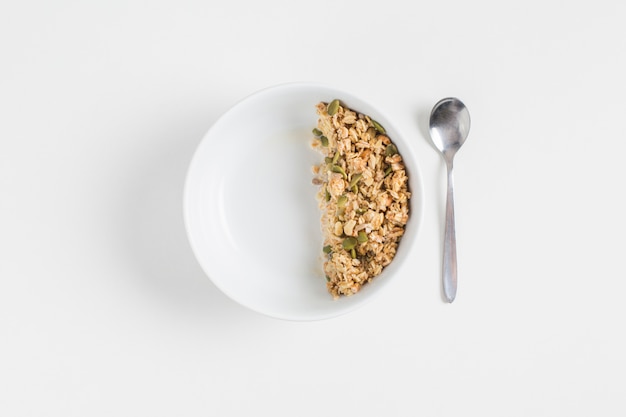 Granola avec des graines de citrouille dans un bol blanc et une cuillère sur un fond blanc