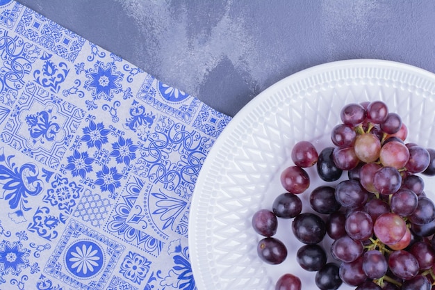 Une grappe de raisin dans une assiette blanche sur une table bleue.