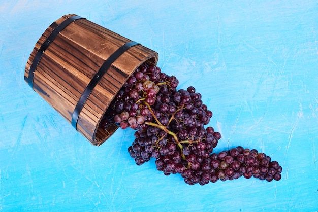 Une grappe de raisin rouge dans un seau en bois sur bleu, vue de dessus.