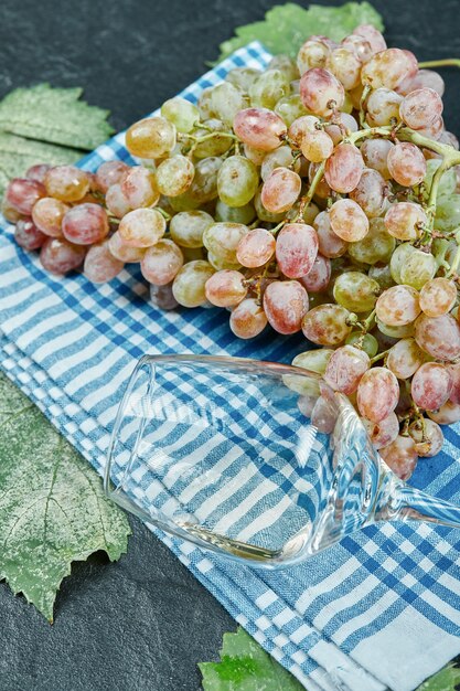 Une grappe de raisin rouge et un verre à vin sur une nappe bleue. Photo de haute qualité