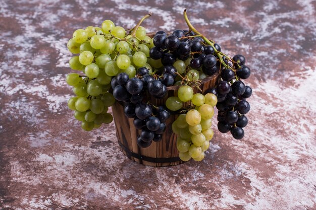 Une grappe de raisins verts et rouges dans le seau au milieu sur le marbre