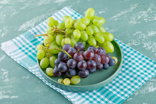 Photo gratuite grappes de raisins dans un bac vue grand angle sur fond de plâtre et tissu de pique-nique