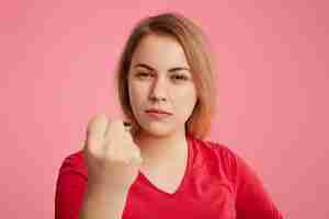 Photo gratuite grave femme en colère lève le poing alors qu'il essaie de vous avertir, vêtue d'un pull rouge