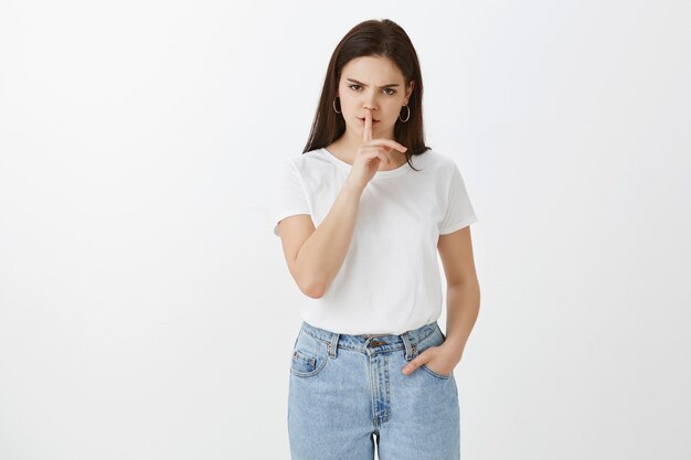 Grave irritée jeune femme posant contre le mur blanc