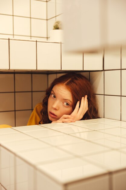 Grave jeune femme rousse bouclée assis dans un café sous la table