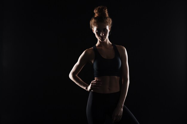 Grave jeune femme sportive debout sur un mur noir