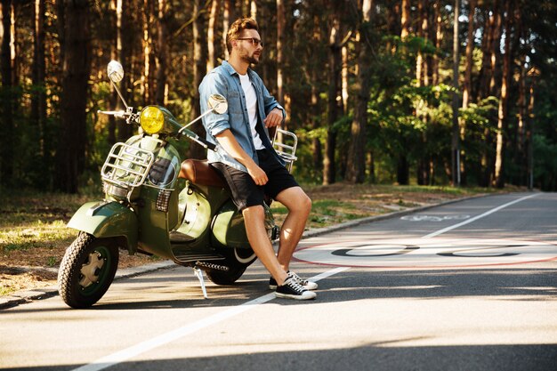 Grave jeune homme barbu debout près de scooter