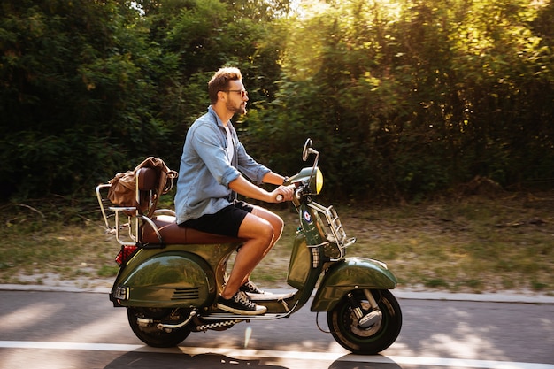 Grave jeune homme barbu sur scooter à l'extérieur.