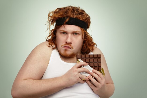 Greedy obèse gros jeune homme portant un groupe de sport sur les cheveux roux bouclés