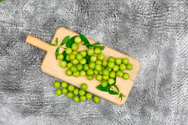 Greengages avec des feuilles dans une planche à découper sur gris grungy. vue de dessus.