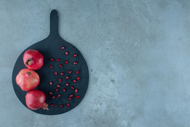 Grenade et graines rouges sur un plateau noir.