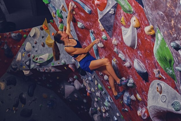 Grimpeuse professionnelle sur un mur de bloc à l'intérieur.