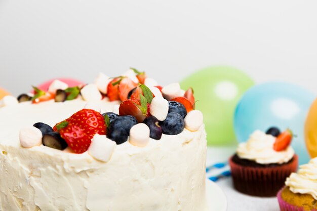 Gros gâteau avec différentes baies près de cupcakes sur la table