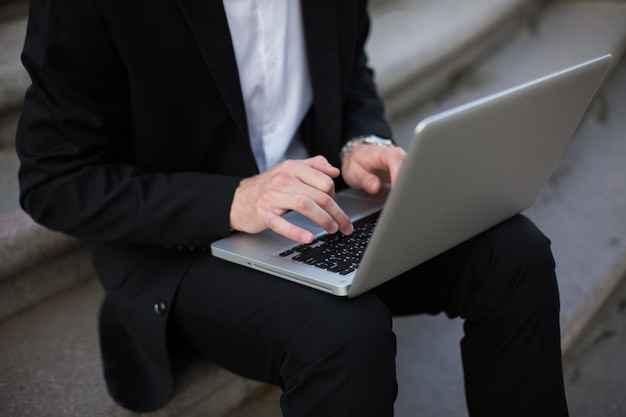 Gros homme d'affaires en costume noir classique travaillant sur un ordinateur portable en plein air