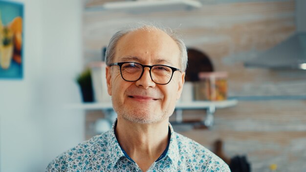 Gros homme senior souriant dans la cuisine regardant la caméra avec des lunettes. Portrait d'une personne âgée détendue le matin, dégustant une boisson chaude et fraîche. Visage adulte souriant en bonne santé